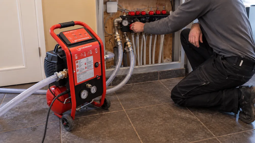 Monteur spoelt de vloerverwarming bij de verdeler
